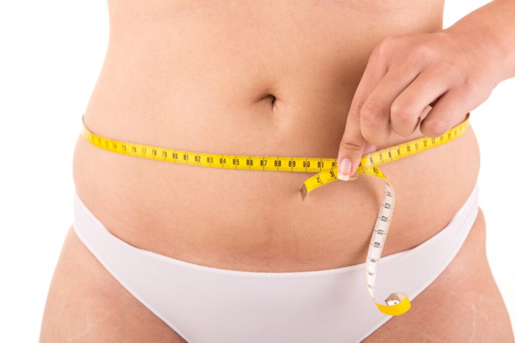 Closeup of woman measuring her naked waist with tape measurer before having fat reduction in Sebring, FL